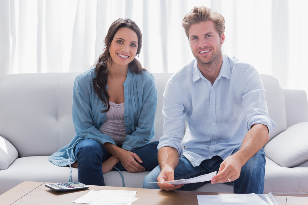 Happy couple sitting down on a couch with bills or papers