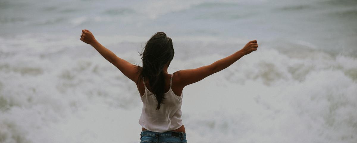 Woman with stretched arms in front of the ocean