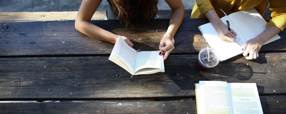 People sitting at a table and reading books outside