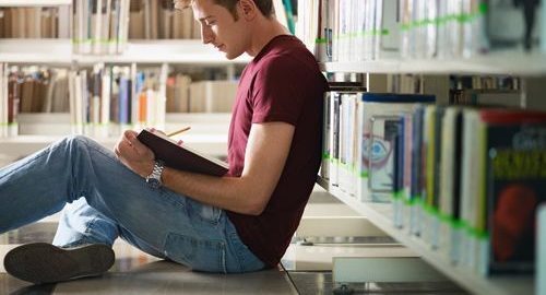 Student sitting down and reading a book in a library