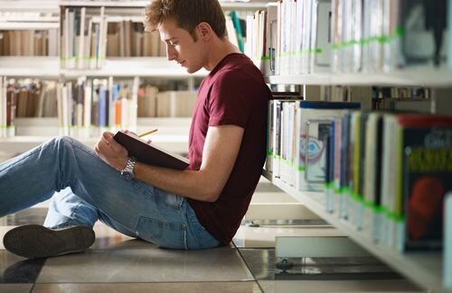 Student sitting down and reading a book in a library
